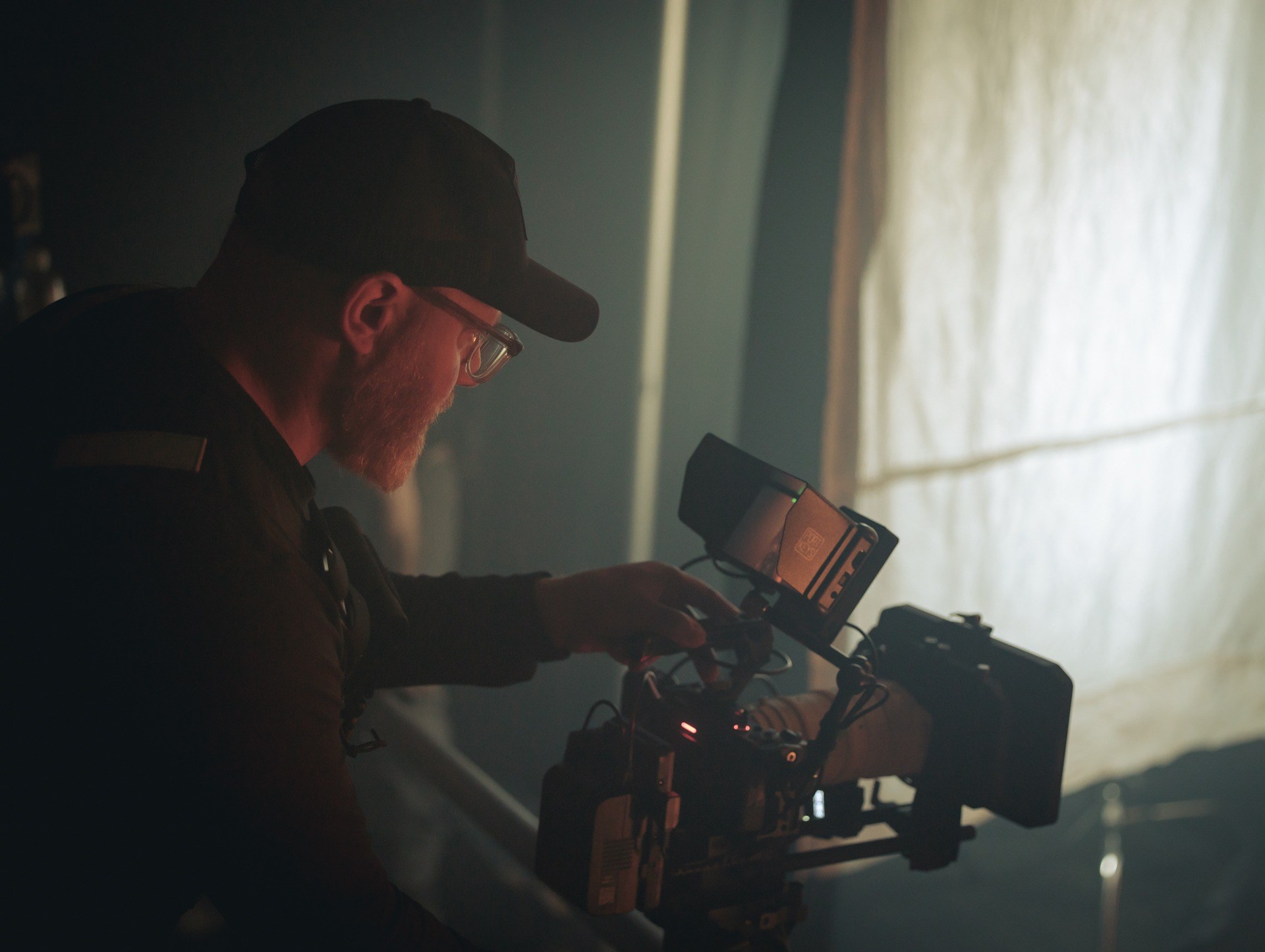 A single videographer filming with a cinema camera in natural window light on location in BC