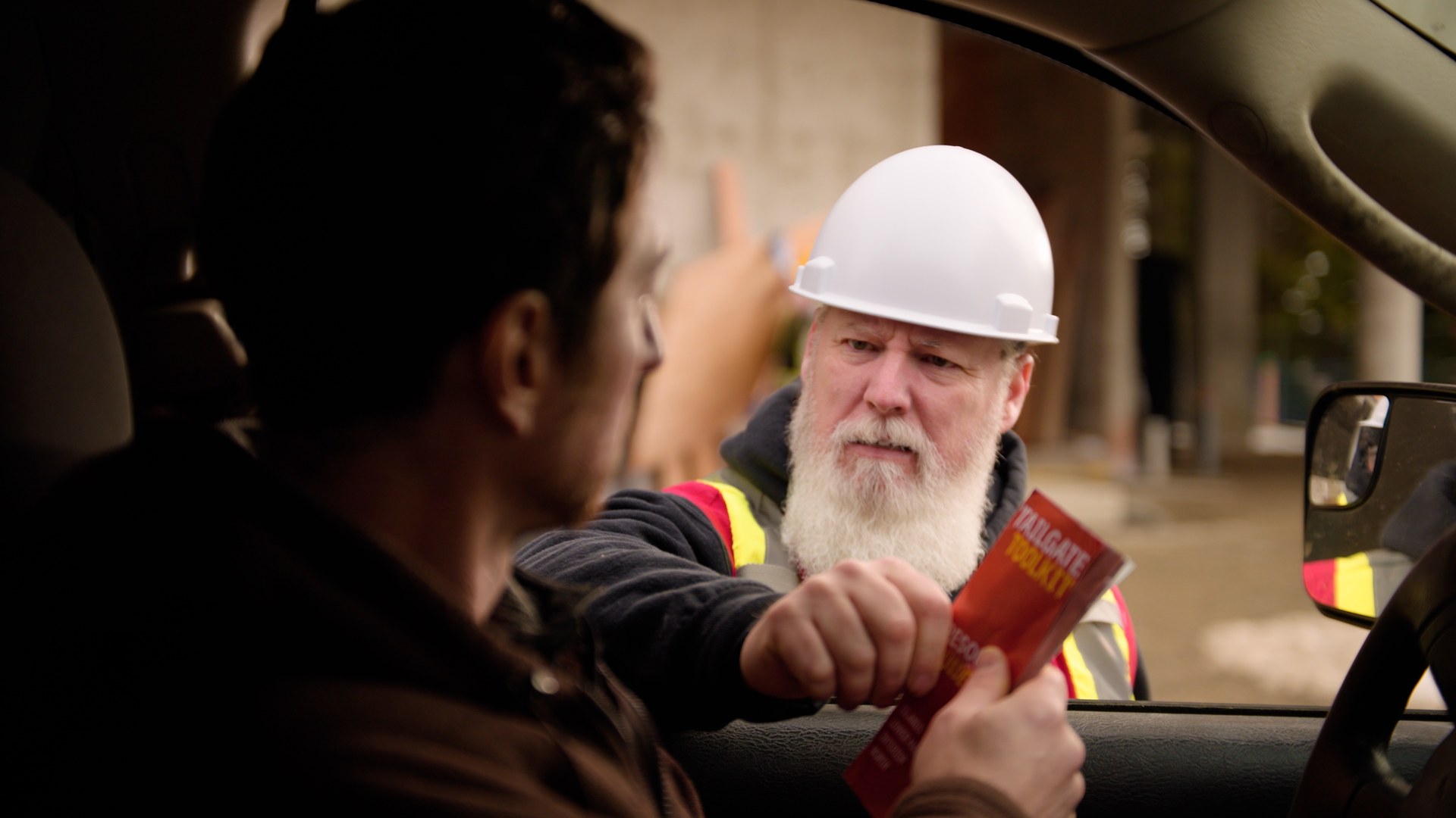 The supervisor hands a Tailgate Toolkit resource guide to a worker through the truck window